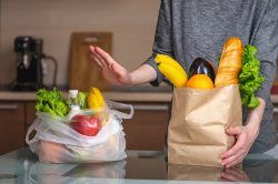 A hand giving a "no" gesture to groceries in a plastic bag