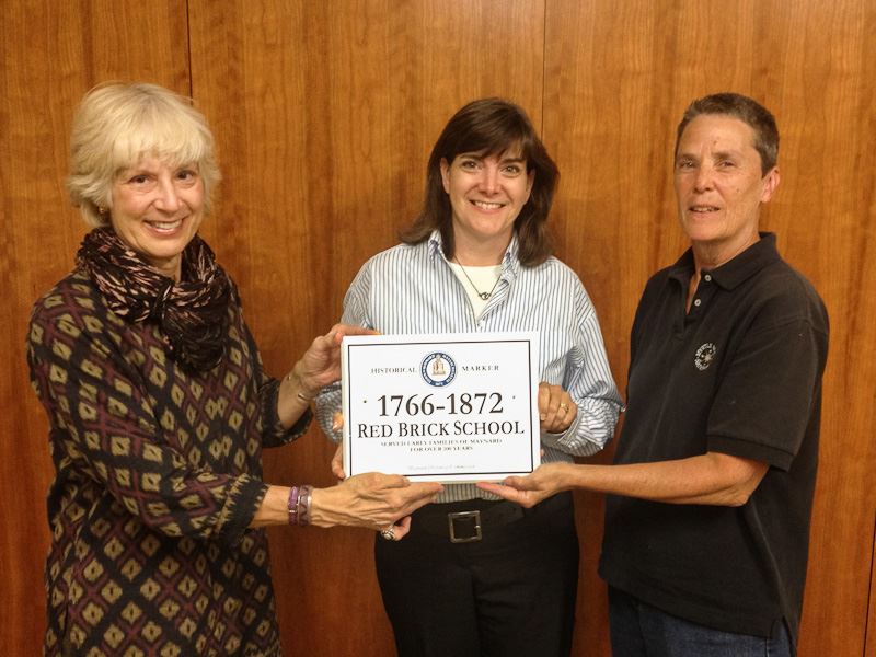 Three people holding a sign that says 1766-1872 Red Brick School