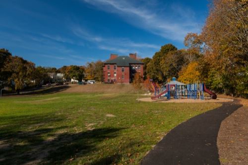 A playground next to some trees with a house in the background